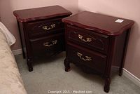 Pair of dark reddish-brown wooden night stands, each with two drawers and brass handles, showing carved legs and curved top edges.