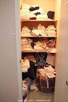 Full shelving unit filled with assorted linen items including towels, sheets, and tablecloths stacked on four shelves.