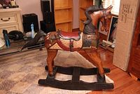 Front-left side view of the wooden carousel rocking horse showing decorative carved and painted details and the rocking base