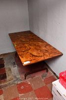 Side angle showing full length of folding table with wood-grain top and metal legs against a concrete wall.