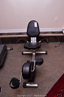 Front and side view of the Free Spirit recumbent stationary bike showing black padded seat, backrest, handlebars, and pedals on silver metal frame.