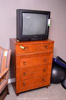 Side angle of wooden four drawer dresser with 26-inch Mitsubishi TV on top, showing the dresser's wood grain and wear, TV curved screen and front control panel