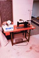 Overview of vintage sewing machine on wooden table with metal frame; box of sewing supplies on left side of table
