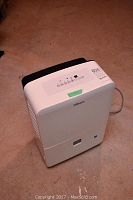 Full view of white and black dehumidifier on concrete floor.