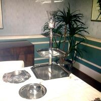 Three tier silverplate serving tower with glass candle holder and separate silverplate base with glass bowl lid seen on table surface.