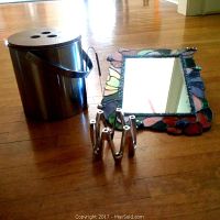 Stainless steel ice bucket with wooden lid, stained glass mirror, and metallic candlestick holder arranged on a hardwood floor
