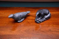 Two Inuit animal sculptures on a wooden surface, showing a seal and a curled polar bear.