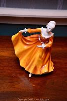 Porcelain Royal Doulton figurine of a dancing lady in an orange dress, seen from a front angle showing full figure and dress detail.