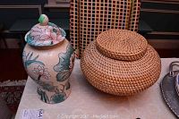 Asian style ceramic vase with floral motifs next to woven wicker basket with lid on table.