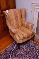 Full view of the wing back chair showing the seat, arms, and wooden legs on a patterned rug.
