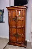 Full view of wooden armoire with four paneled doors closed under a mounted TV
