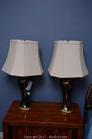 Pair of bronze lamps with white shades on a wooden cabinet against blue wall