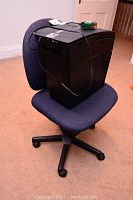 Office chair with blue cushioned seat and backrest, black plastic base with five caster wheels, holding the shredder