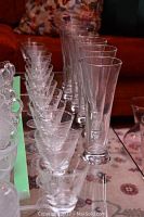 Photo showing 12 small stemmed glasses arranged in a row on a reflective surface with a dark background.
