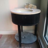 Front angled view of the vanity showing beige marble top, chrome taps, black wooden body and lower round shelf with dust.