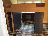 Full view of twin loft bed elevated frame with black supports and natural wood guardrails and side panels in front of a window.