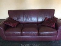 Front view of burgundy leather three-seat sofa with two decorative pillows, showing overall condition and style.