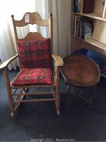 Wooden rocking chair with red cushioned seat pad and oval wooden side table.