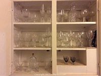 Shelf with crystal and glassware including multiple wine glasses, champagne flutes, a cut crystal decanter with stopper, and two small dark glasses.