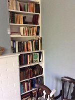 Wide view of most shelves showing the books and some wooden chairs nearby.