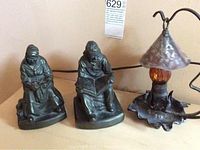 Photo showing both bronze statues and the lamp arranged in a row on a flat surface with lamp cord visible.