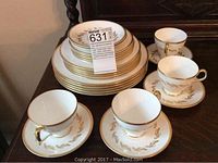 Set of stacked plates, 4 cups placed beside 4 matching saucers on a dark surface