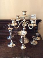 Set of silverplate candlesticks and vase on a wooden surface, including one five-arm candelabra, four individual candlesticks, and one small vase.