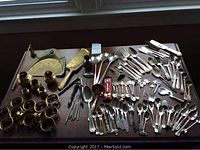 Full view of assorted silver plate and metal items including spoons, forks, napkin rings, candle holders and nutcrackers arranged on table