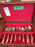 Opened case showing red felt interior with multiple slots containing forks, spoons, and utensils.