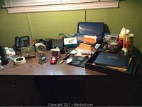 Wide view of desk with assorted phones, clocks, model truck, and office supplies spread out