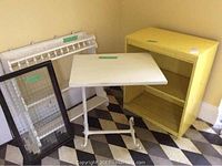 Photo of small shelf unit, rolling tray table, hanging shelf, and framed glass grouped on floor with checkered tile pattern background.