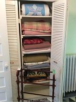 Photo showing folded blankets and quilts stacked on shelves inside a closet, with wooden quilt rack leaning in front.