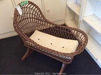 Wicker baby rocking cradle with cushion from a top-down angle, showing the woven wicker design and cushion inside.