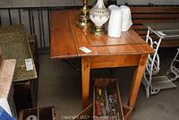 Side view of rustic wooden table with one drop leaf extended and one drawer underneath, showing wood grain and wear.