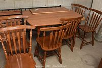 Wide shot of dining table, leaf extension placed on top, and six chairs around.