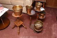 Lot showing 5 brass pots on two wooden plant stands in living room setting.
