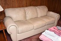 Front view of three-seat beige leather sofa against wood panel wall with lamp and side table