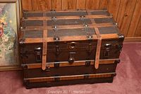 Front view of trunk showing wood slats, metal panels, leather straps and metal hardware.
