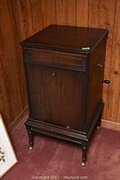 Full view of the dark wood phonograph cabinet with decorative trim and four legs with casters.