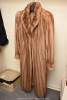 Full view of the blonde mink fur coat hanging on a hanger showing length and overall condition.