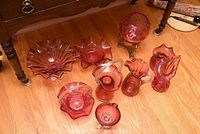 Front angle showing all nine cranberry glass items on wood floor under table