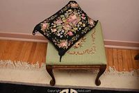 Full view of needlepoint stool with floral cushion on top, showing part of the wooden legs and needlepoint fabric