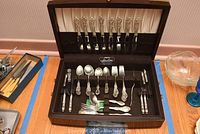 Open wooden chest showing full flatware layout with loose pieces