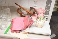 Overview showing glass salad bowl with wooden utensils, four clear glasses, linens in shades of pink and floral, pink ceramic tea set pieces, green creamer, and white dishware.