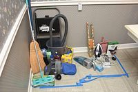 Photo showing the entire lot grouped together, with brooms, bucket, mop, vacuums, iron, and dustpan visible