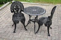 Full view of black wrought iron bistro set on patio pavers—round table and two chairs