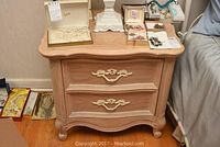 Front view of one pickled finish Lexington end table showing two drawers with brass handles and carved feet.