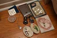 Overall top-down view of all items: compact, cloth, cigarette cases, necklace, earrings, rings, trinket box and bead set