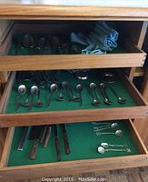 Top drawer open showing assorted spoons, forks, and bone-handled knives on green felt lining inside wooden drawer