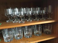 Two-tier shelf showing about 12 stemmed goblets above and 6 old fashioned tumblers below